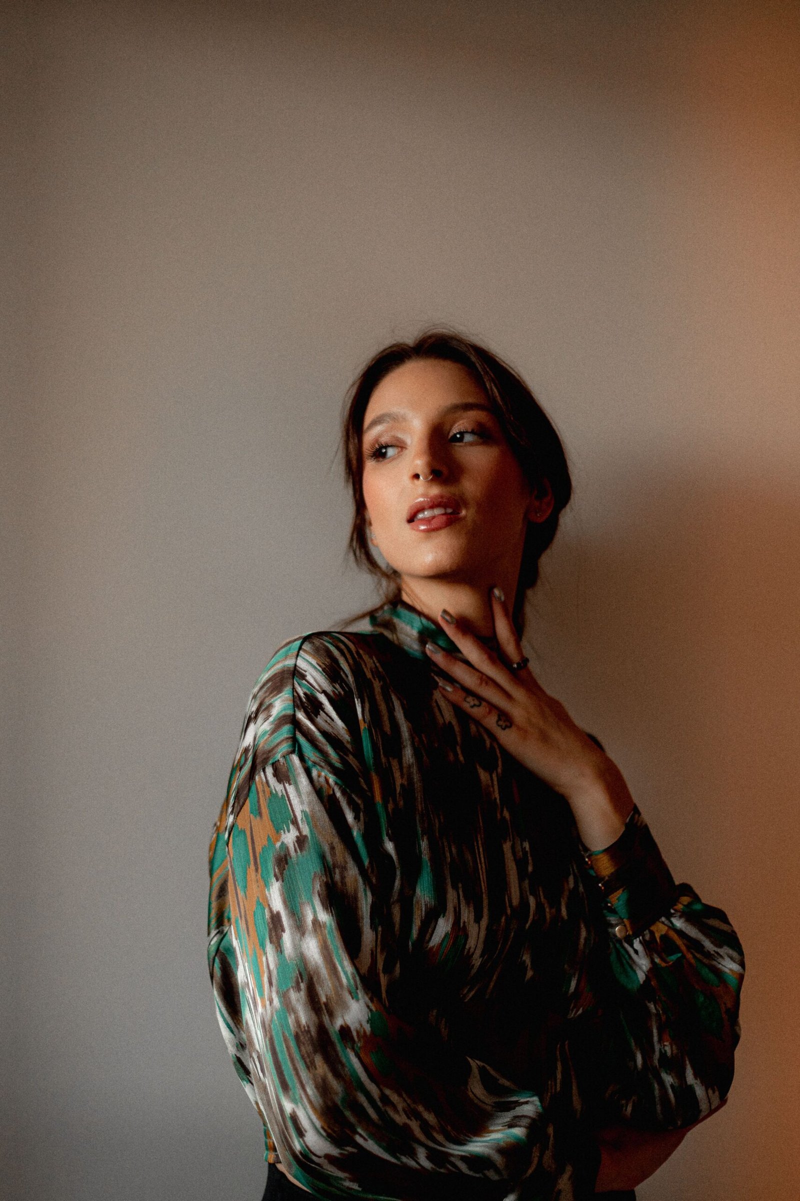 Elegant woman in floral-patterned blouse posing indoors with hand on neck.